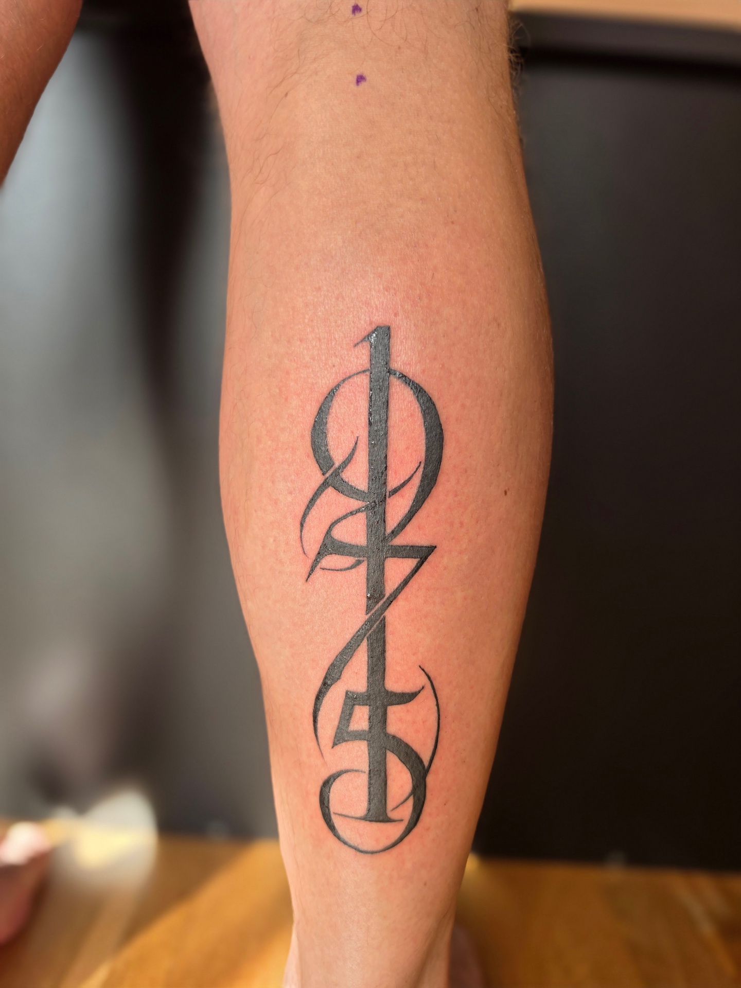 Melnas monogrammas tetovējums uz apakšdelma, tetovētāja Krista Jansone